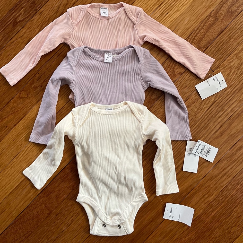 Set of three organic baby girl bodysuits.